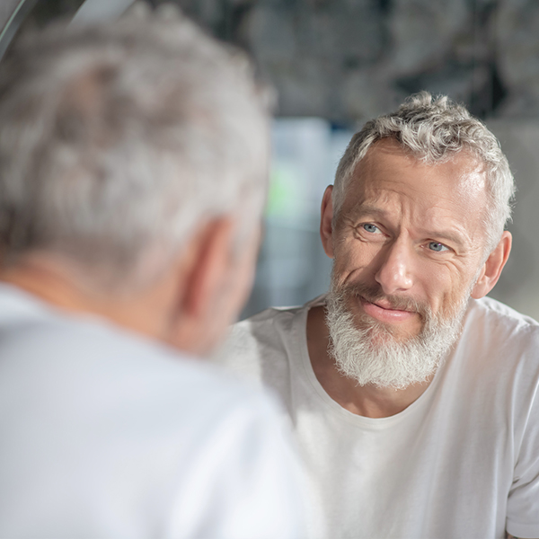 http://Gray%20haired%20man%20with%20a%20beard%20looks%20at%20his%20reflection%20in%20a%20mirror